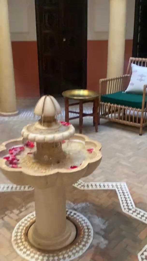 Table ronde en zellige vert et fauteuils en rotin dans le patio d'un riad