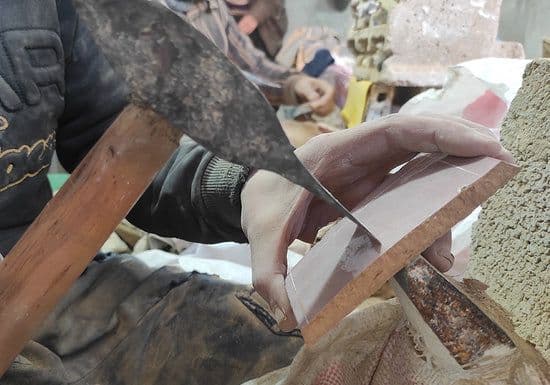 Artisan marocain façonnant à la main une pièce de zellige traditionnel.